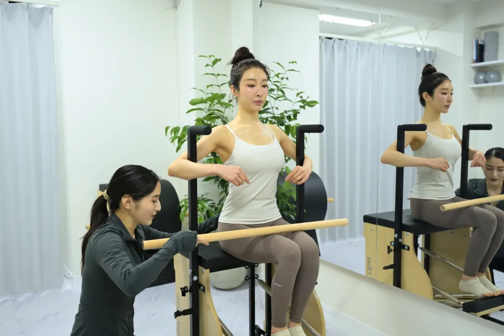 銀座Pilates Beautéのプライベートスタジオで、インストラクターがマンツーマンでチェアの姿勢を指導する様子